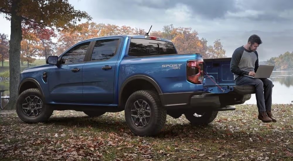 A person sitting on the bed of a blue 2024 Ford Ranger XLT Sport is shown while using a laptop.