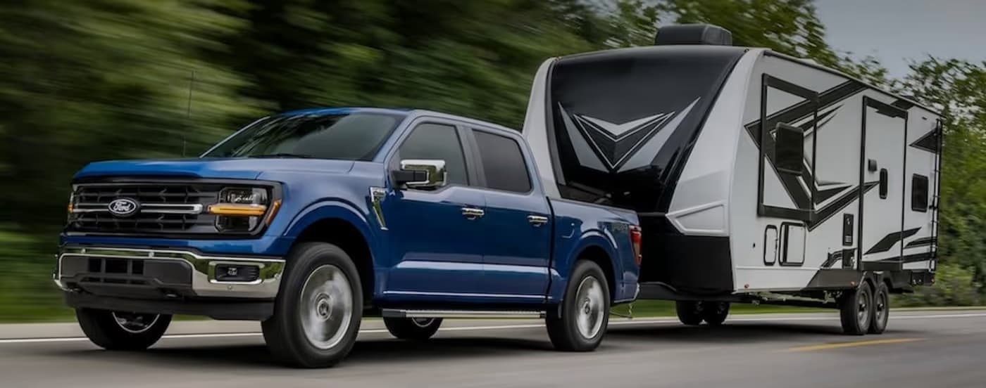 A blue 2025 Ford F-150 STX towing a trailer.