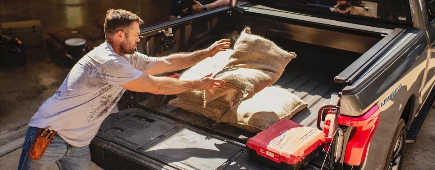 A person is shown throwing a sack into the bed of a gray 2024 Ford F-150 Lightning.