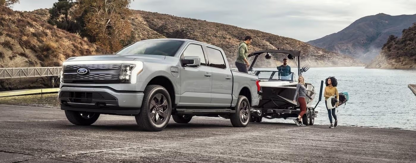 A silver 2024 Forf F-150 Lightning is shown towing a boat near water.
