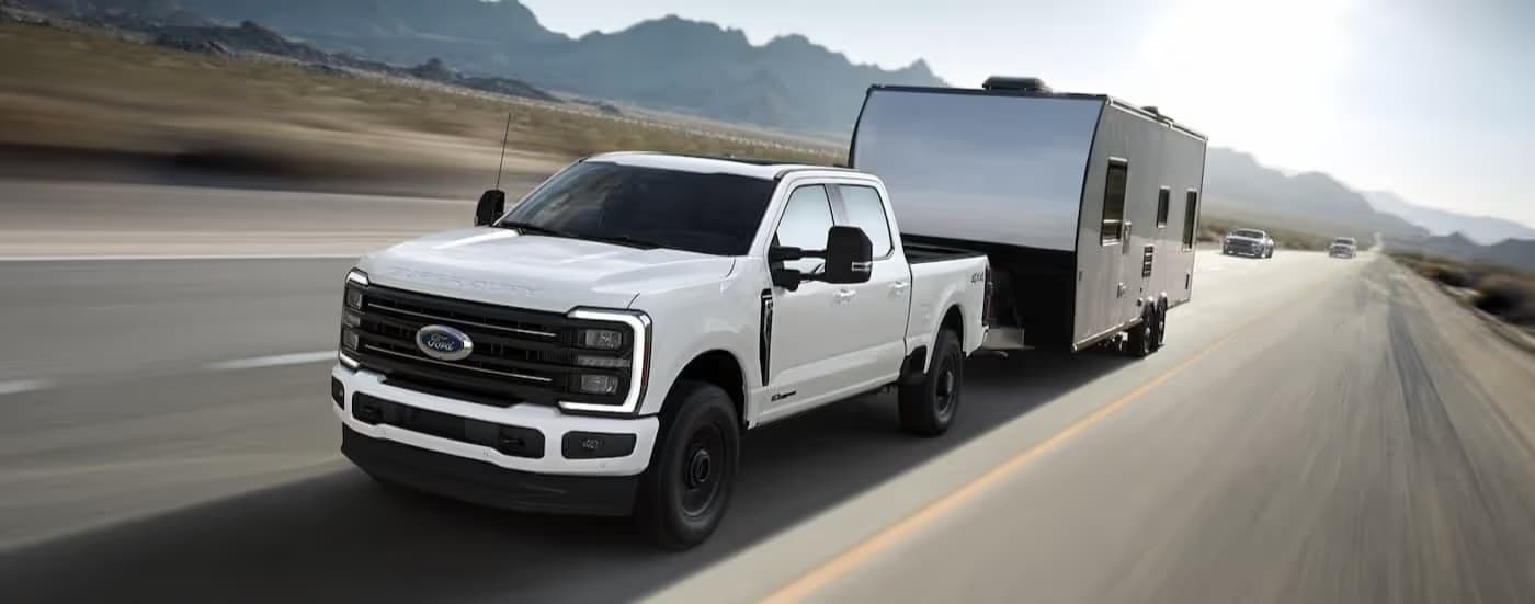 A white 2025 Ford F-350 towing a trailer on a highway.