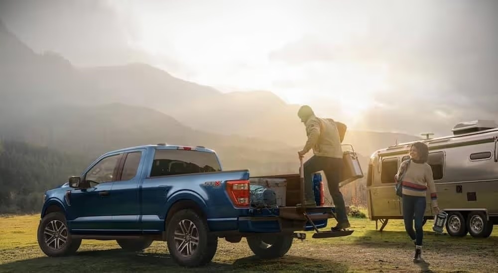 A blue 2023 Ford F-150 Lariat is shown parked near mountains.