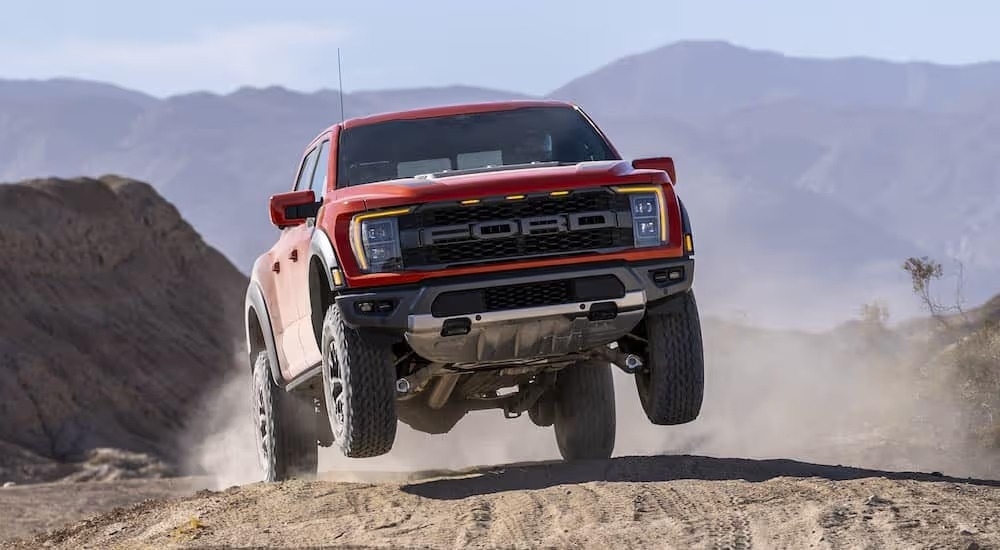 A red 2021 Ford F-150 Raptor is shown from the front while jumping off-road.