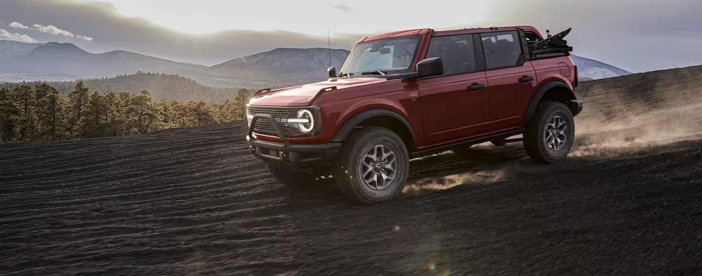 A red 2024 Ford Bronco is shown from the side driving on a dirt area.