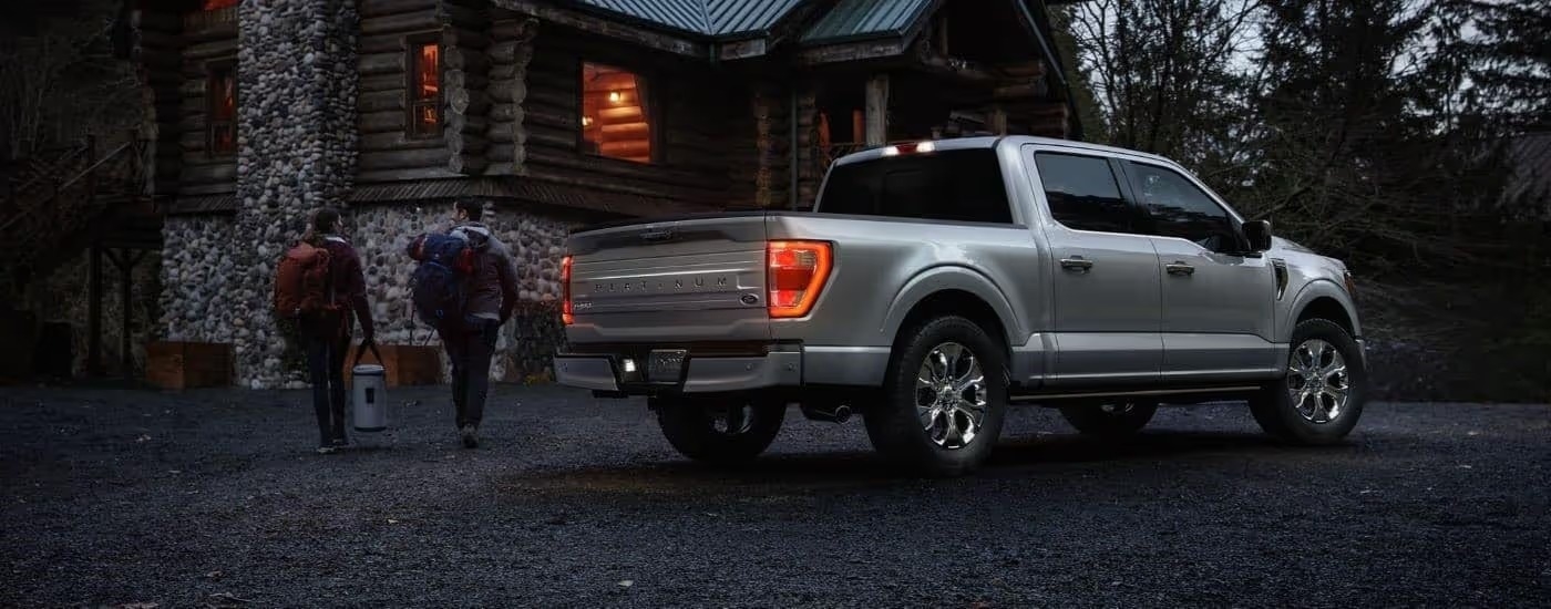 A silver 2023 Ford F-150 Platinum is shown from the rear parked next to a cabin at night.