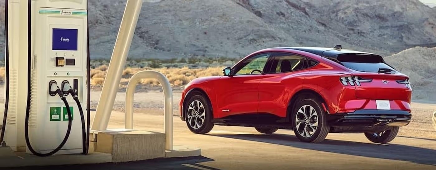 A red 2023 Ford Mustang Mach-E is shown parked near a charge station.