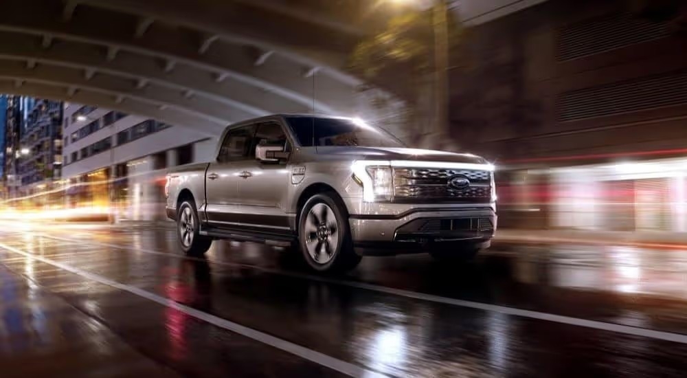 A silver 2024 Ford F-150 Lightning is shown driving through a rainy tunnel.