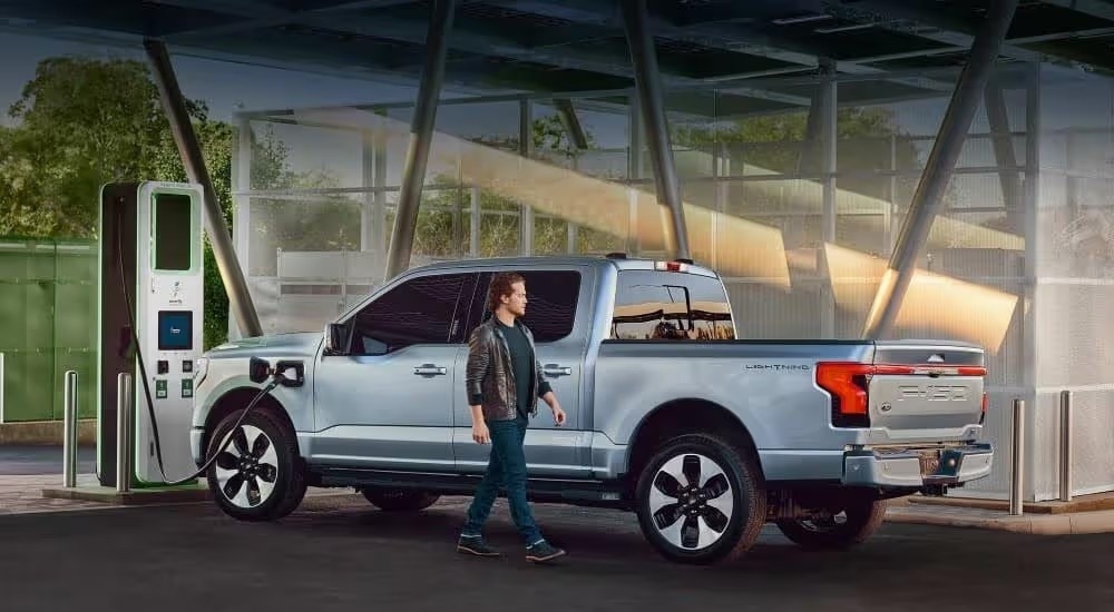 A light blue 2024 Ford F-150 Lightning is shown charging at a charging station.