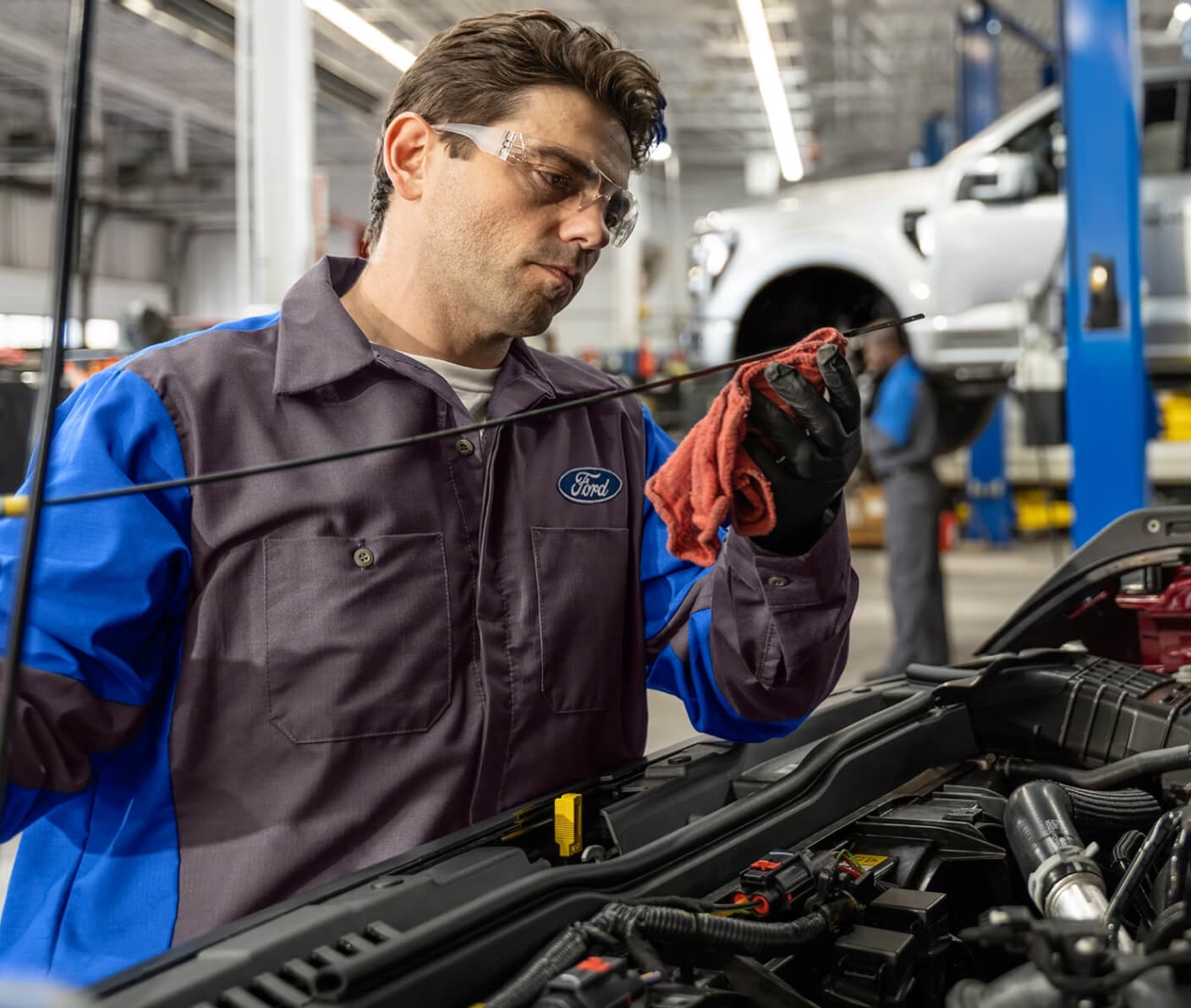 A Ford technician checking an engine oil dipstick inside a dealership service bay.