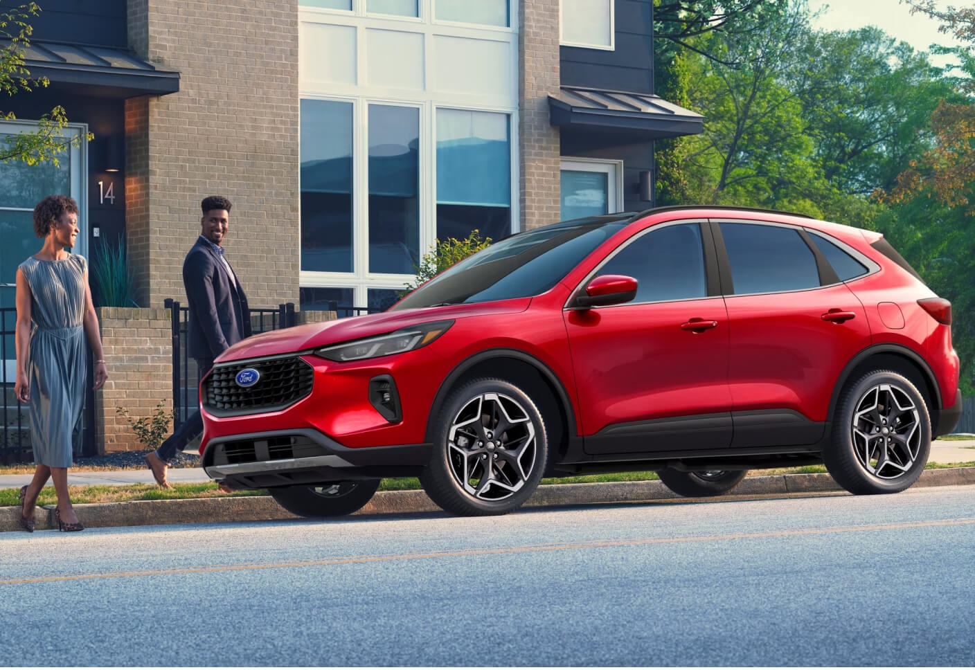 Three-quarter view of a Ford Escape ST-Line Elite in Rapid Red with a couple walking nearby on a suburban street.