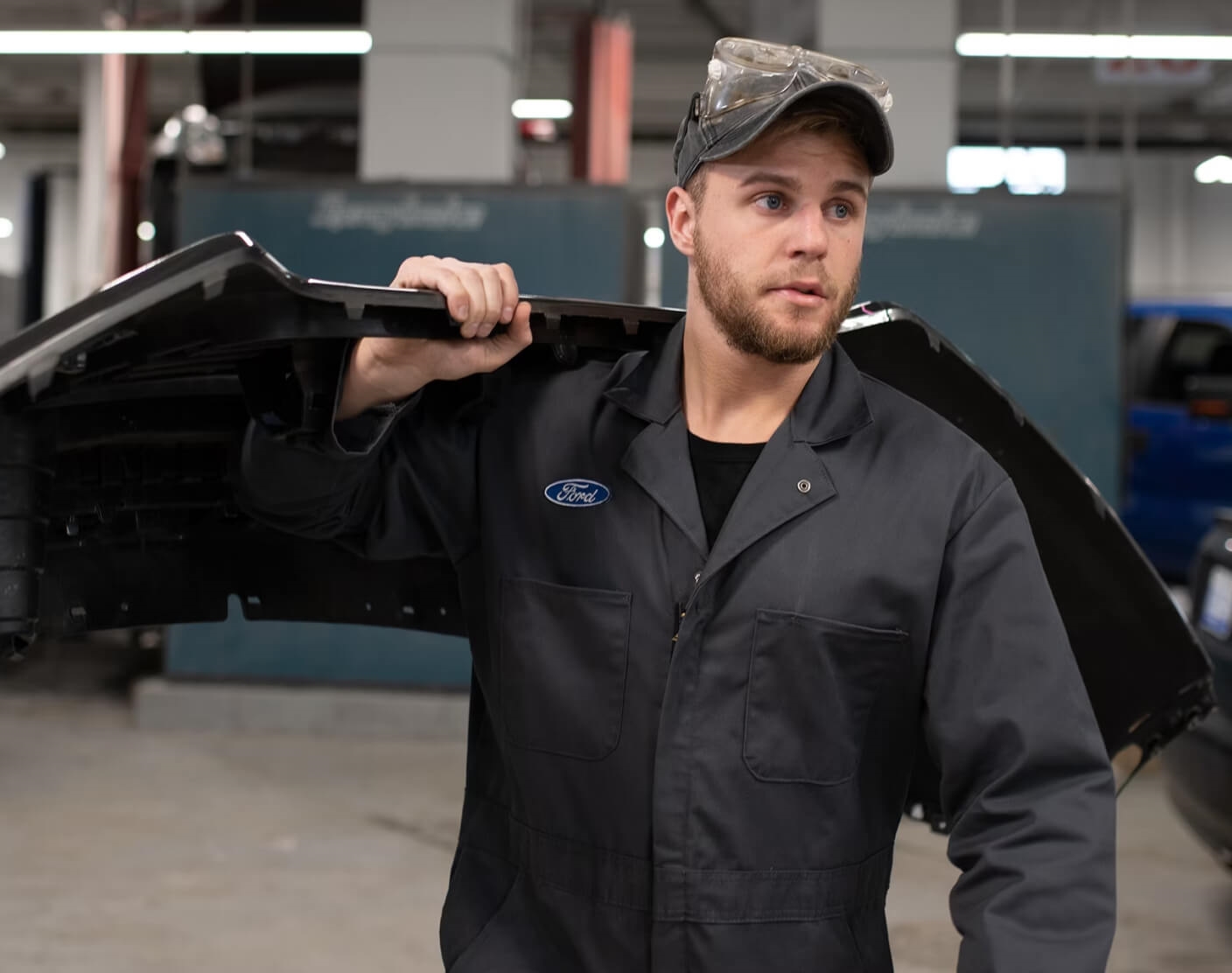 A Ford technician carrying a black bumper cover on his shoulder.