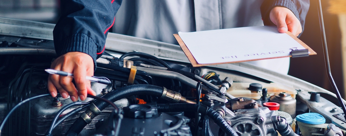 A technician holding a service checklist while working on an engine.