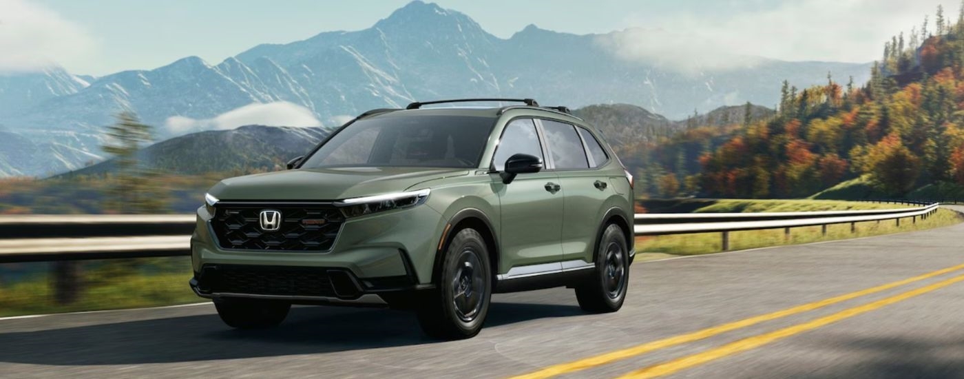 A green 2026 Honda CR-V TrailSport shown driving by a guard rail.