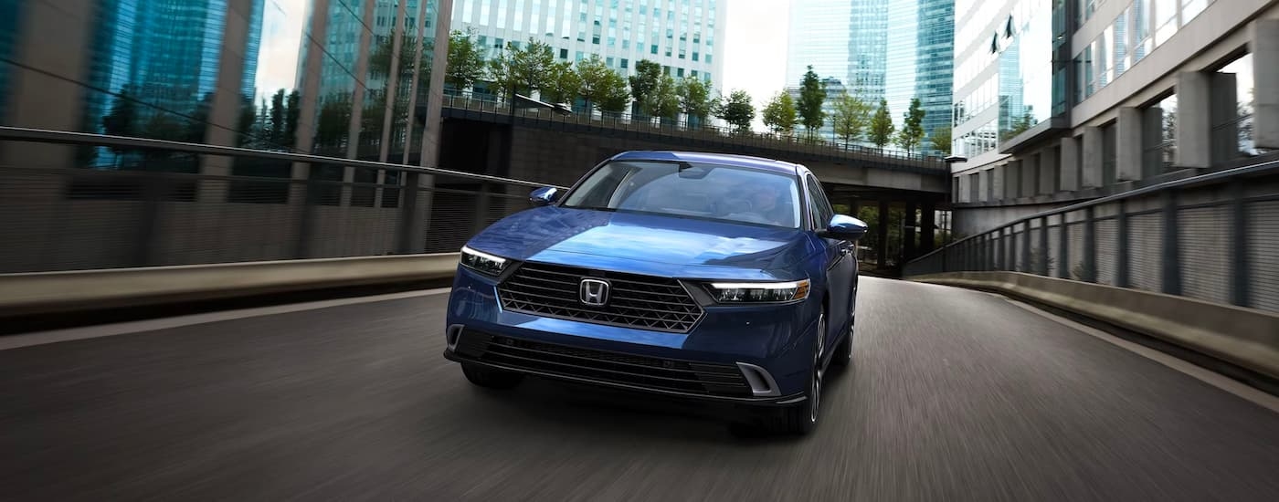A blue 2023 Honda Accord Touring Hybrid crossing a city bridge.