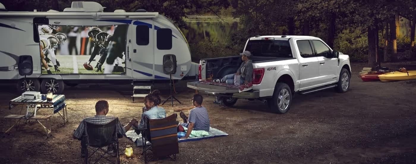 A white 2024 Ford F-150 towing a trailer on a campground.