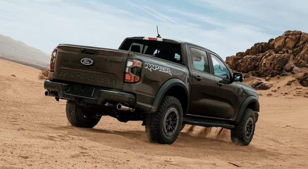 Rear view of a black 2024 Ford Ranger Raptor driving through sandy terrain.
