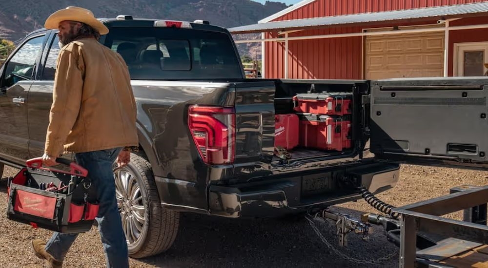 Man walks away from 2025 Ford F-150 STX with toolbox in hand and trailer connected to the truck.