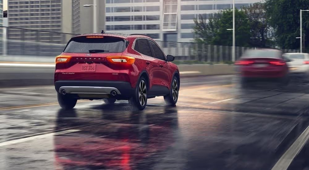 A red 2025 Ford Escape Platinum is shown from rear driving on a city street.