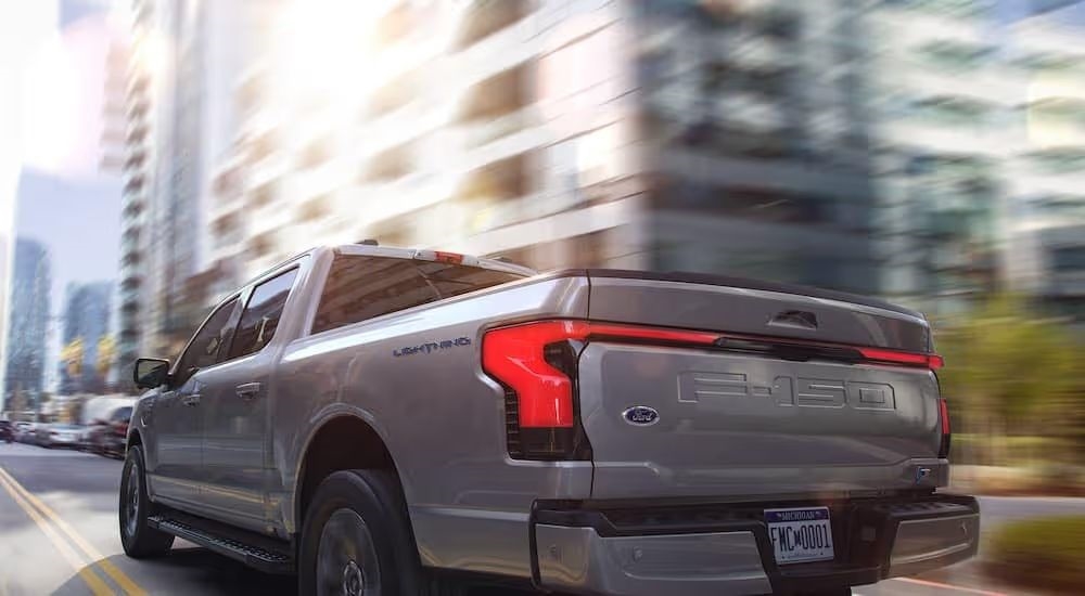 A silver 2025 Ford F-150 Lightning is shown from the rear driving in a city.