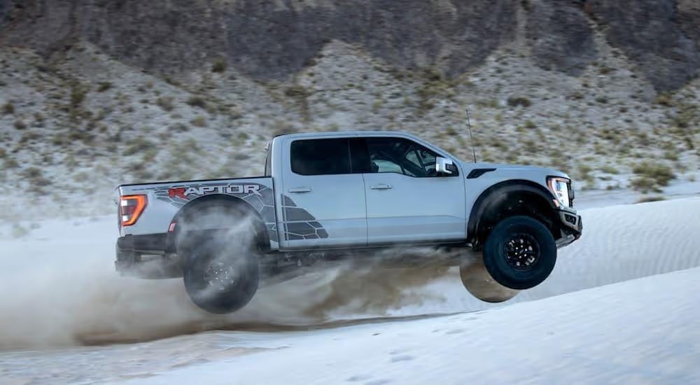 A silver 2025 Ford F-150 Raptor R is shown driving in a sand pit.