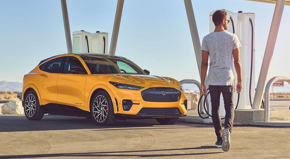 A bright orange 2024 Ford Mustang Mach-E GT parked by a charger.