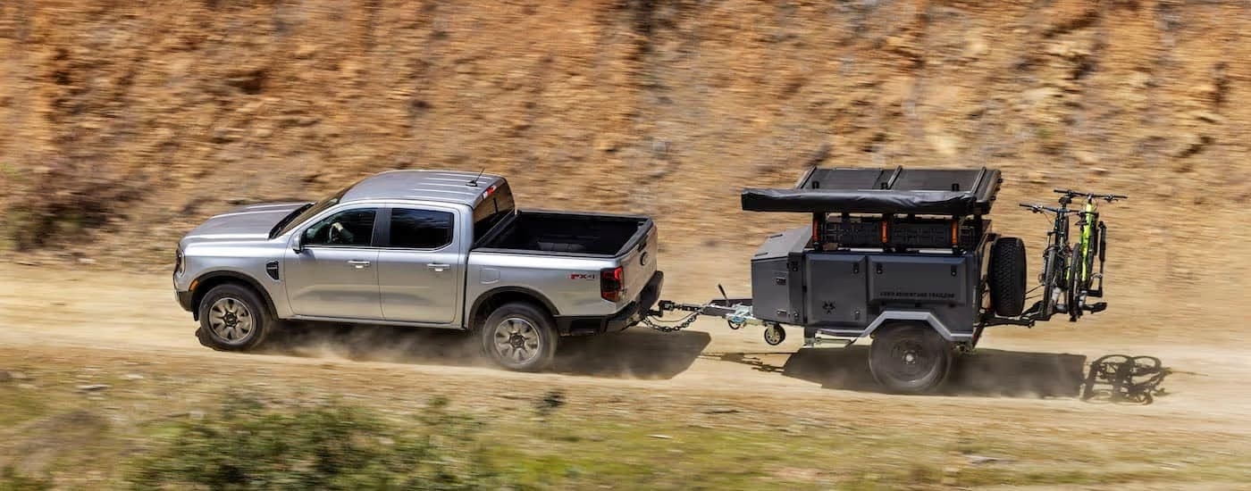 A silver 2024 Ford Ranger towing a trailer offroad.