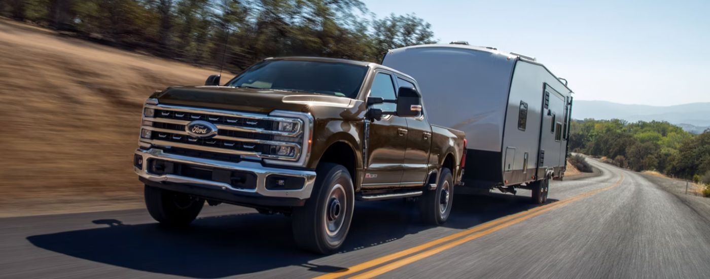Brown 2026 Ford Super Duty towing a camper on a paved road.