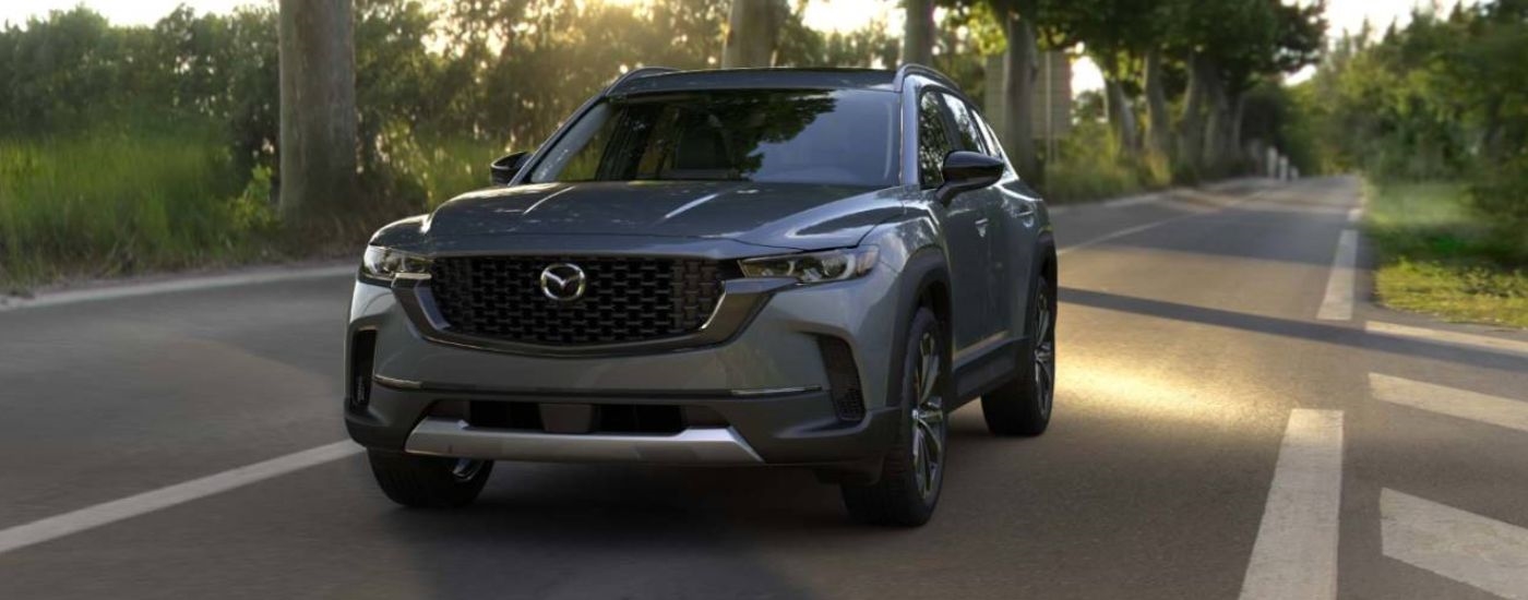 A gray 2026 Mazda CX-50 shown driving a tree-lined road.