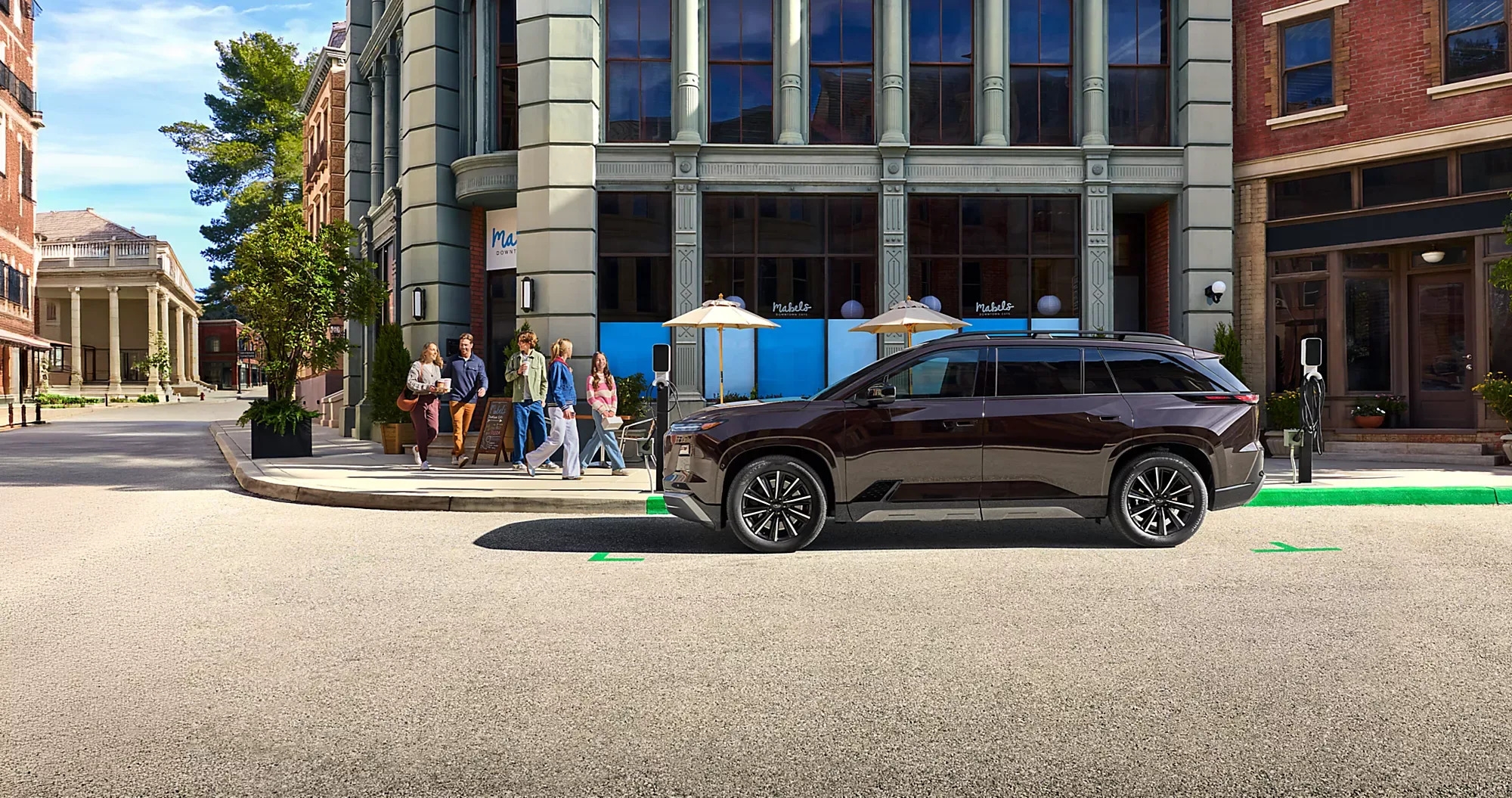 Side profile of the 2027 Subaru Getaway parked on a downtown street beside an EV charger.