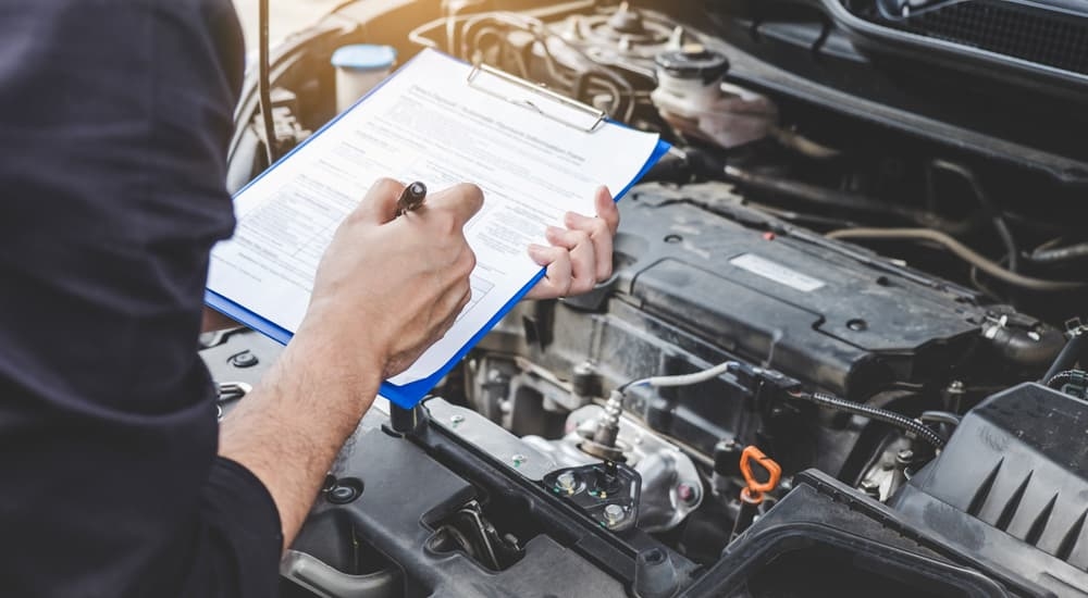A service technician with a clipboard looking over an engine compartment.