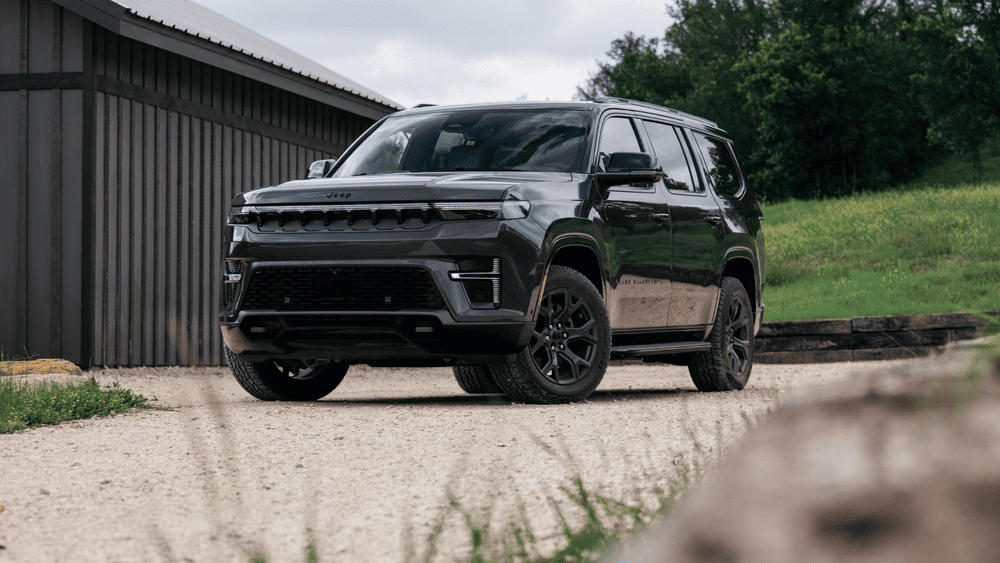 2026 Jeep Grand Wagoneer in Margate FL in all-black with full-width LED lightbar, blacked-out seven-slot grille, black alloy wheels, and running boards parked on a gravel lot