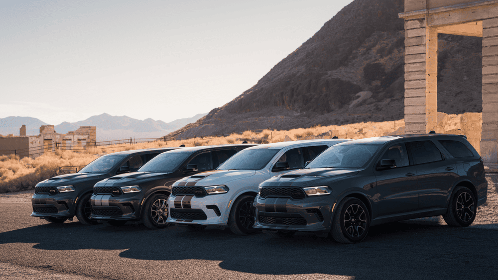Arrigo CDJR of Margate FL new vehicle inventory showing a lineup of Dodge Durango SUVs in gray, black, and silver with SRT racing stripes parked near desert ruins
