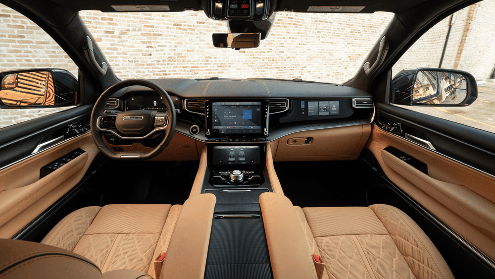 2026 Jeep Grand Wagoneer interior in Margate FL featuring Grand Wagoneer-branded steering wheel, dual center touchscreens, tan quilted leather seats, and black carbon fiber trim