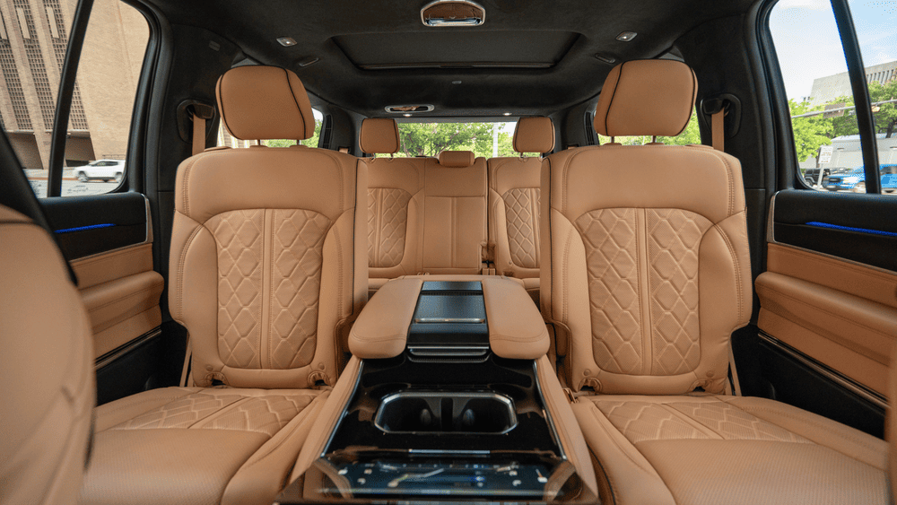 2026 Jeep Grand Wagoneer second-row interior in Margate FL with tan quilted leather captain's chairs, fold-down center console tray, and ambient cabin lighting