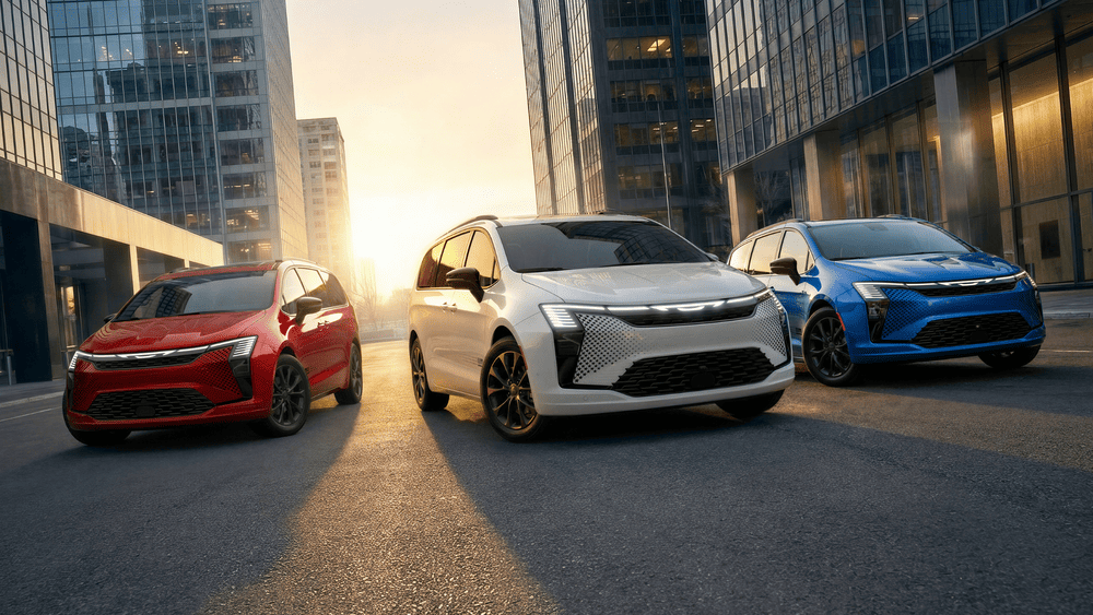 Arrigo CDJR of Margate FL lease inventory featuring red, white, and blue Chrysler Pacifica minivans with illuminated LED grilles lined up in front of a city skyline at sunset