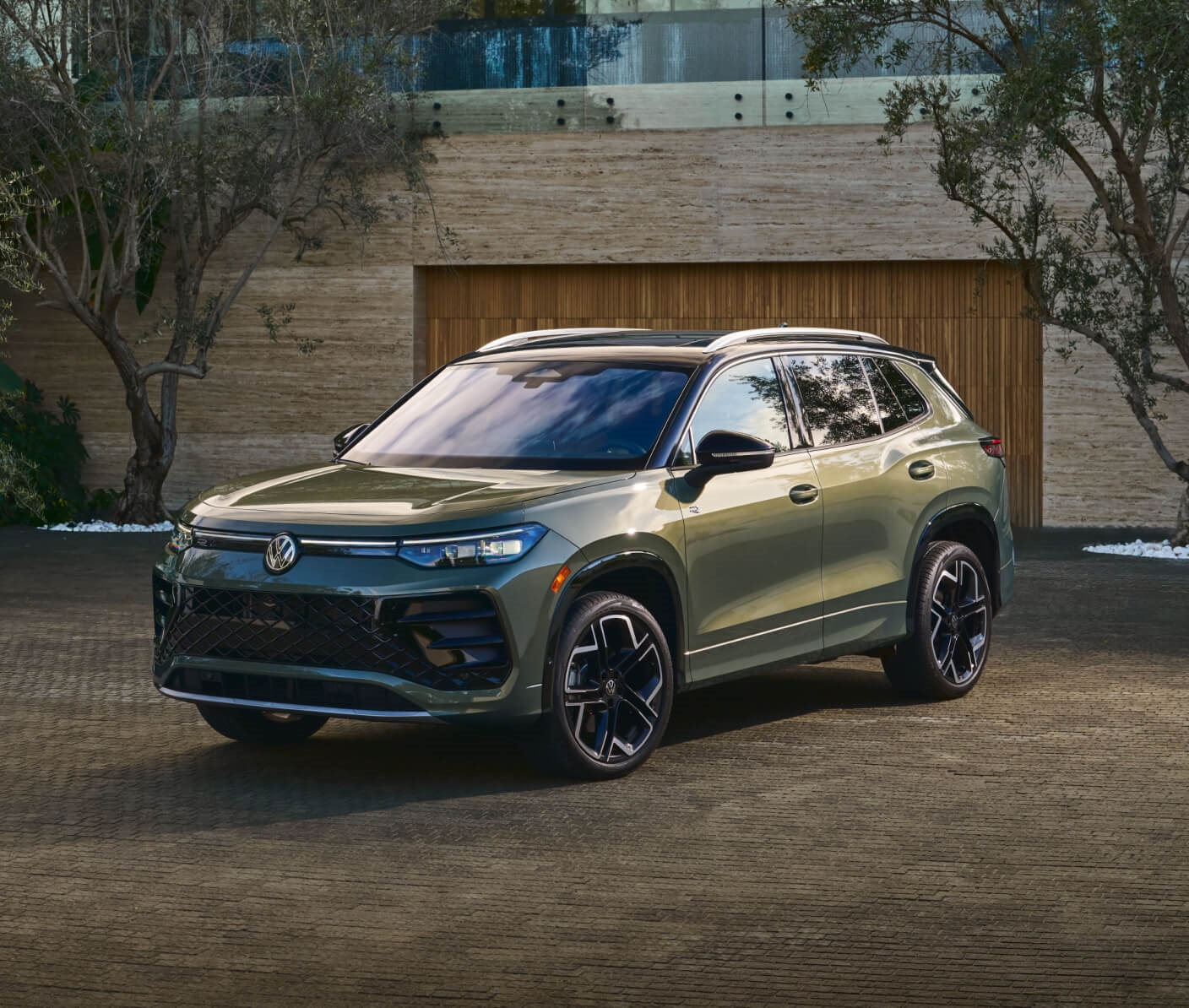 An exterior three-quarter view of a green VW Tiguan parked in the driveway of a modern home.