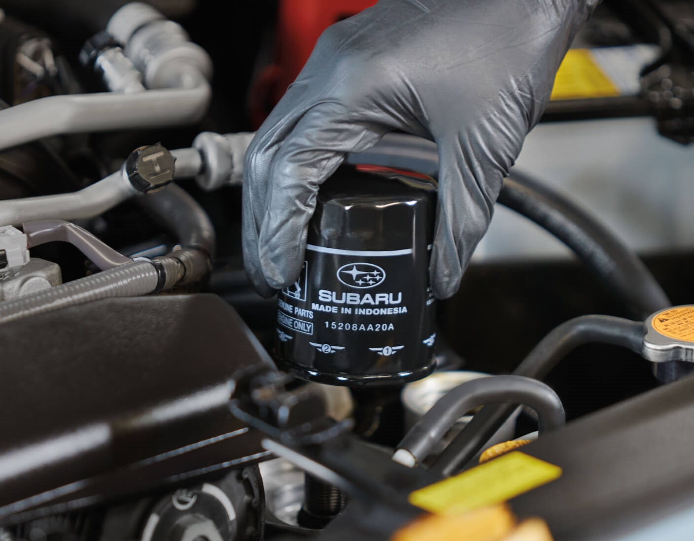 Close-up view of a gloved hand installing a black Subaru OEM oil filter inside an engine.