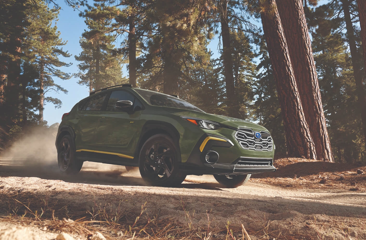 Low-angle view of a green Subaru Crosstrek Sport on a dusty forest trail.