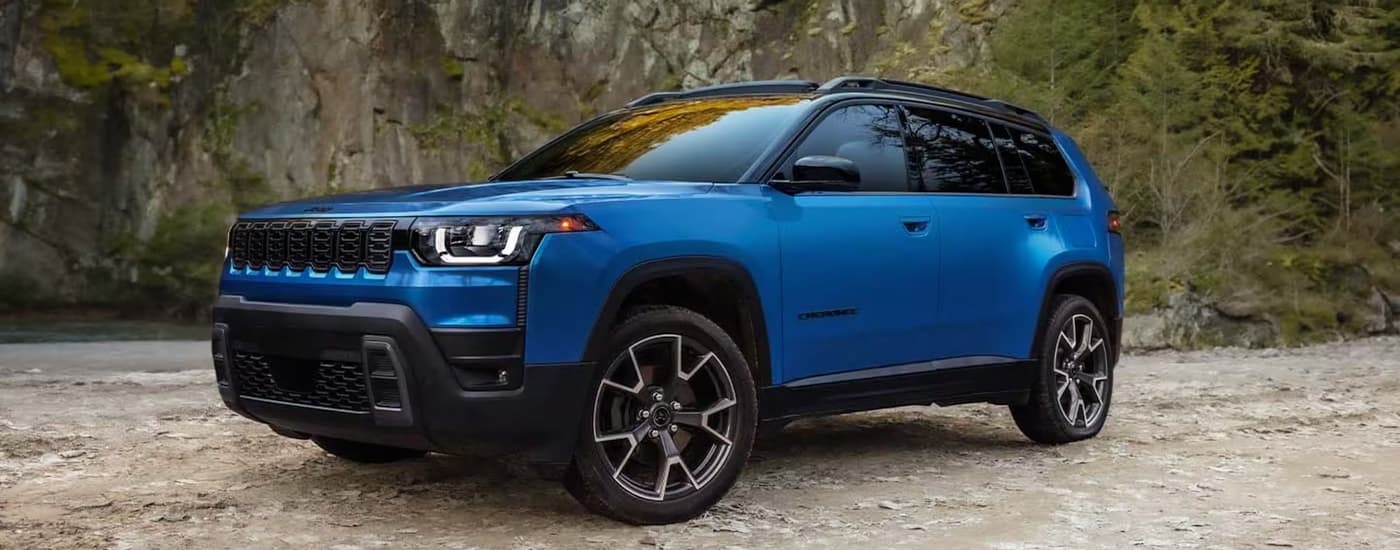 Blue 2026 Jeep Cherokee parked off-road near a lake.