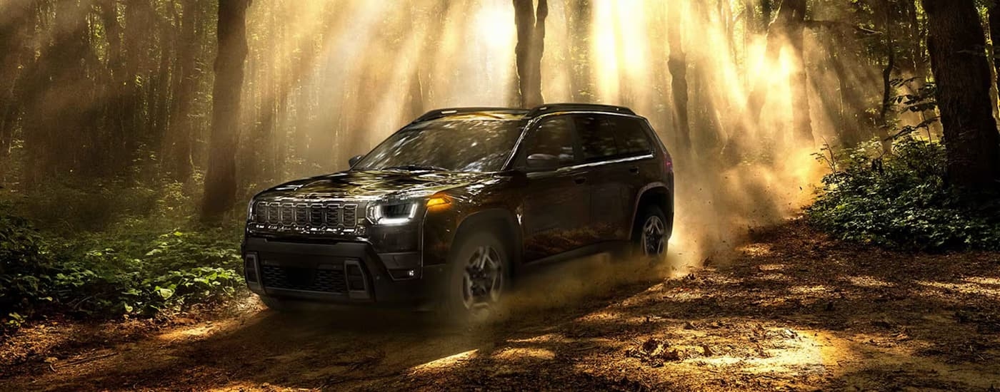 Black 2026 Jeep Cherokee parked off-road in a forest.