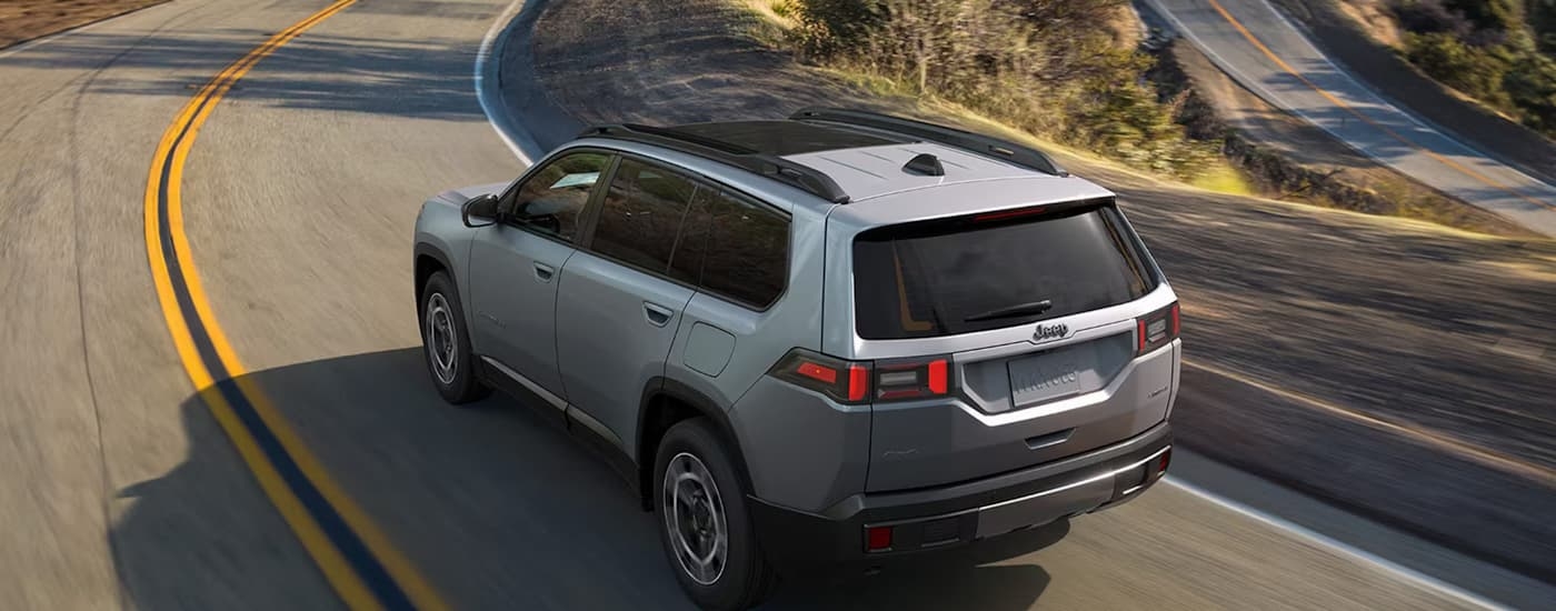 Silver 2026 Jeep Cherokee driving down a winding road.