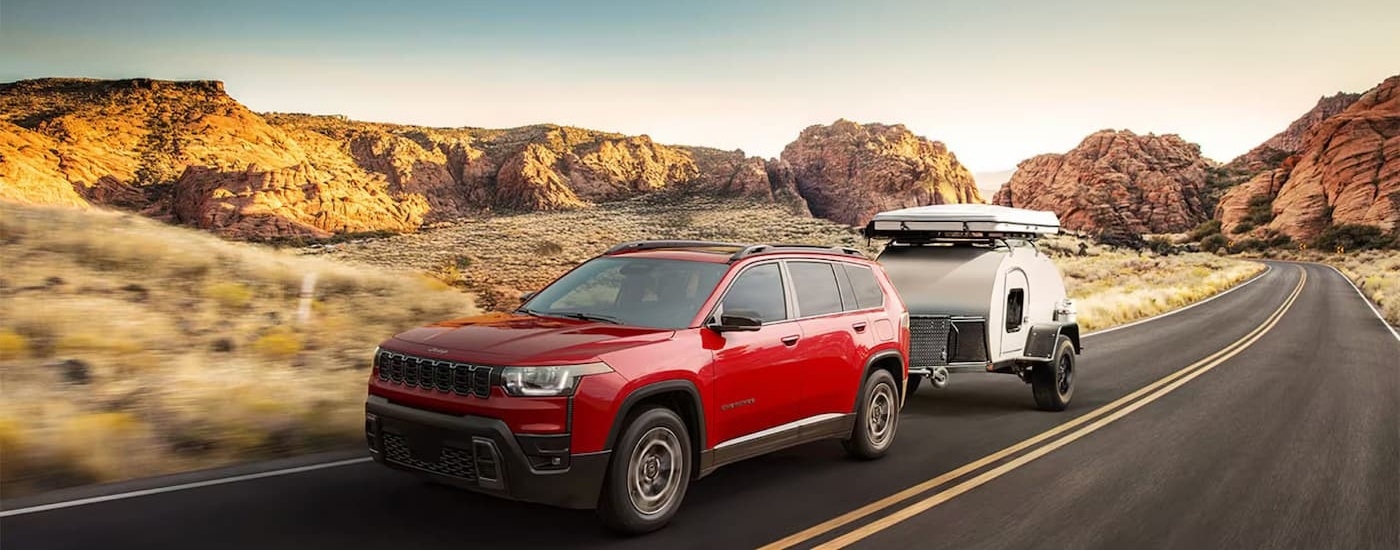 Red 2026 Jeep Cherokee towing a trailer down a road.