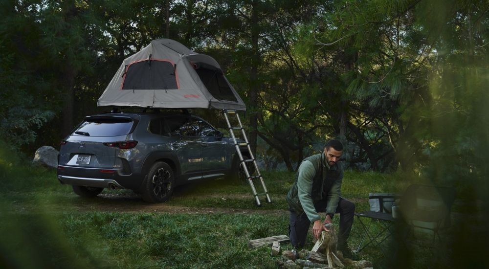 Blue 2026 Mazda CX-50 at a campsite with a tent on the roof.