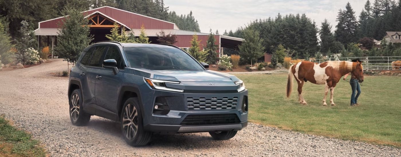 Blue 2026 Toyota RAV4 parked on a farm with a horse in the background.