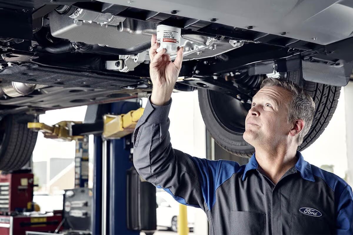 Ford-certified technician performing vehicle maintenance underneath a Ford vehicle in a professional service bay.