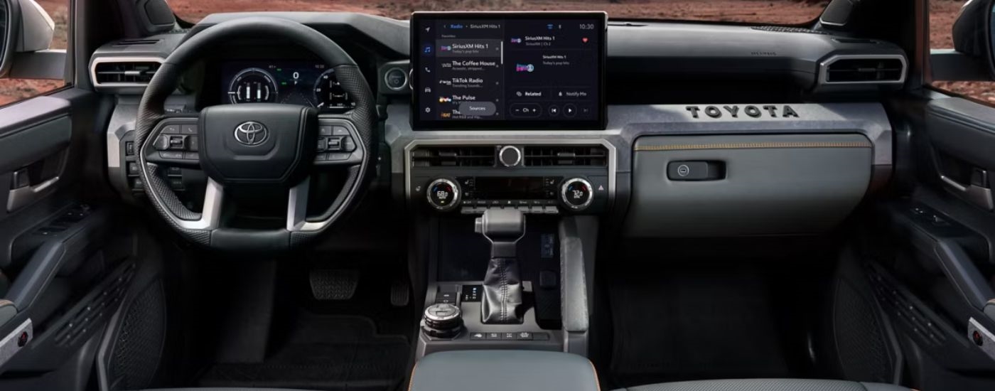 The black front interior of a 2026 Toyota Tacoma showing the steering wheel and infotainment display.