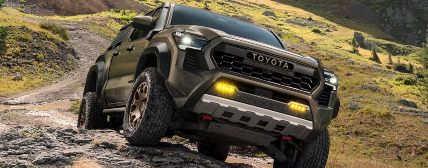 Brown 2026 Toyota Tacoma driving on an off-road dirt trail.