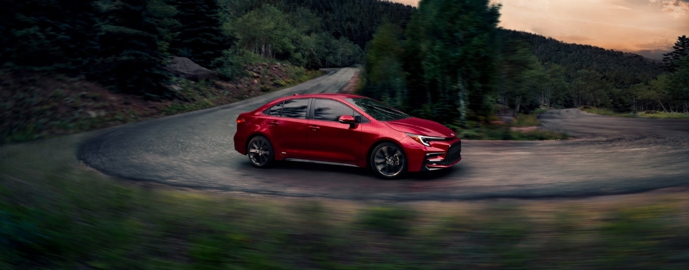 Red 2026 Toyota Corolla driving on a windy road.