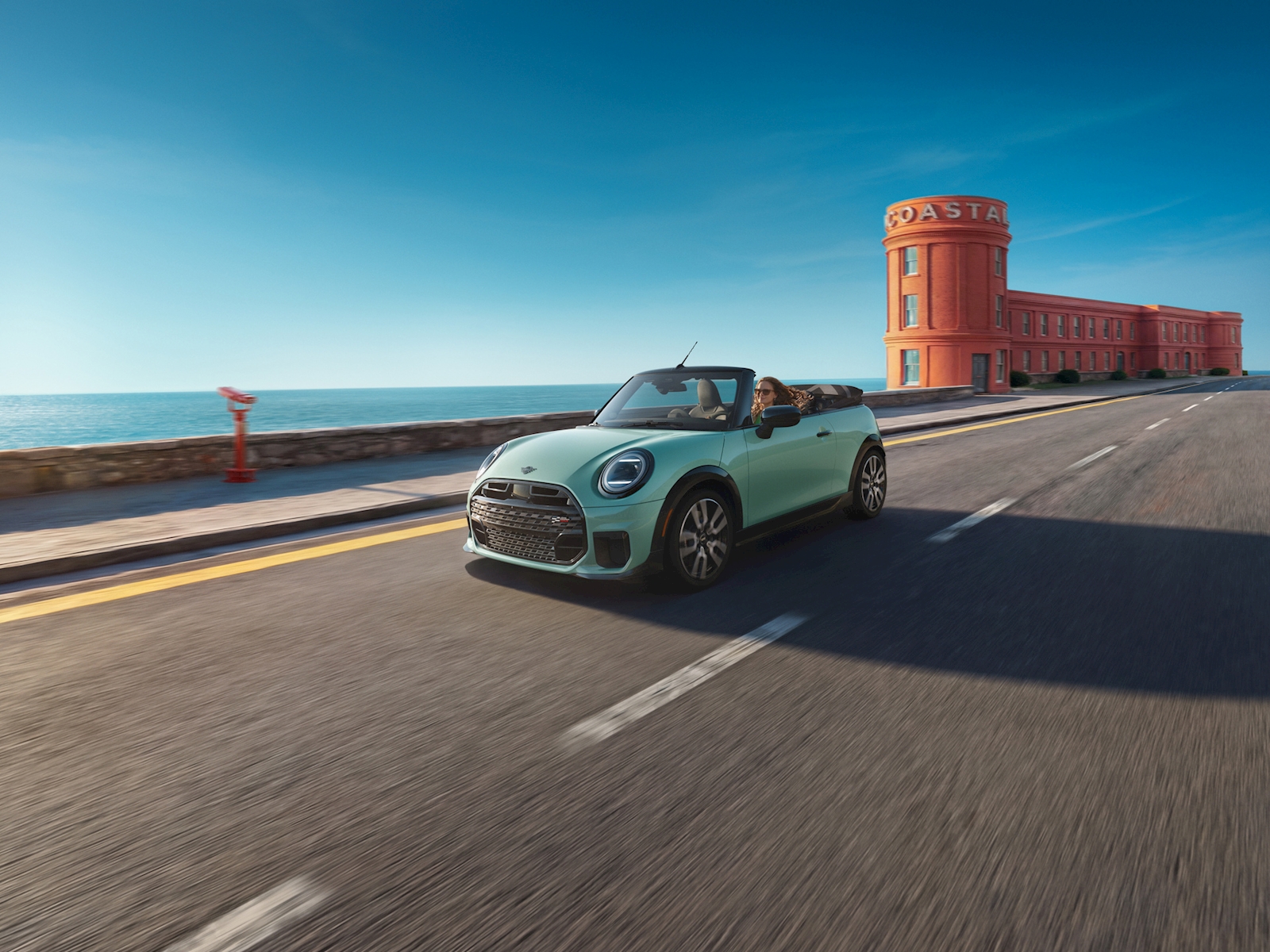 Mint green MINI convertible driving with the top down on a coastal road, available at MINI of Darien