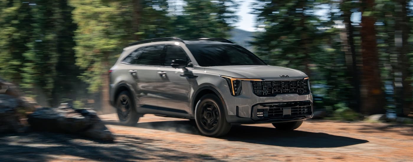 Grey 2026 Kia Sorento driving off-road near a forest.
